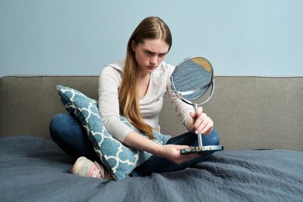 鏡に向かって怒った表情を練習している女性。怒りの感情を表現するトレーニングのイメージ