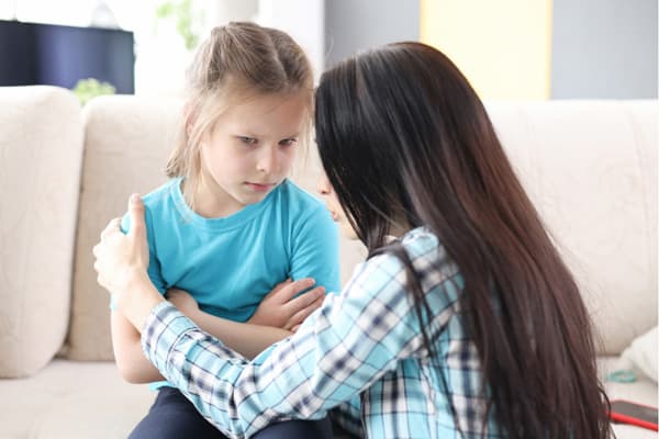 真剣な表情で話しかける母親と、不安そうな娘。家庭内での会話の中で、一方の親への価値観が刷り込まれる様子を表した写真