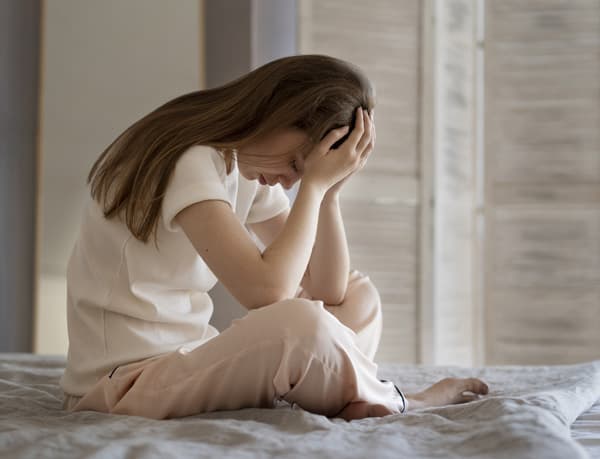 人間関係や自己否定に悩み、心の整理がつかない女性がベッドの上でうなだれている