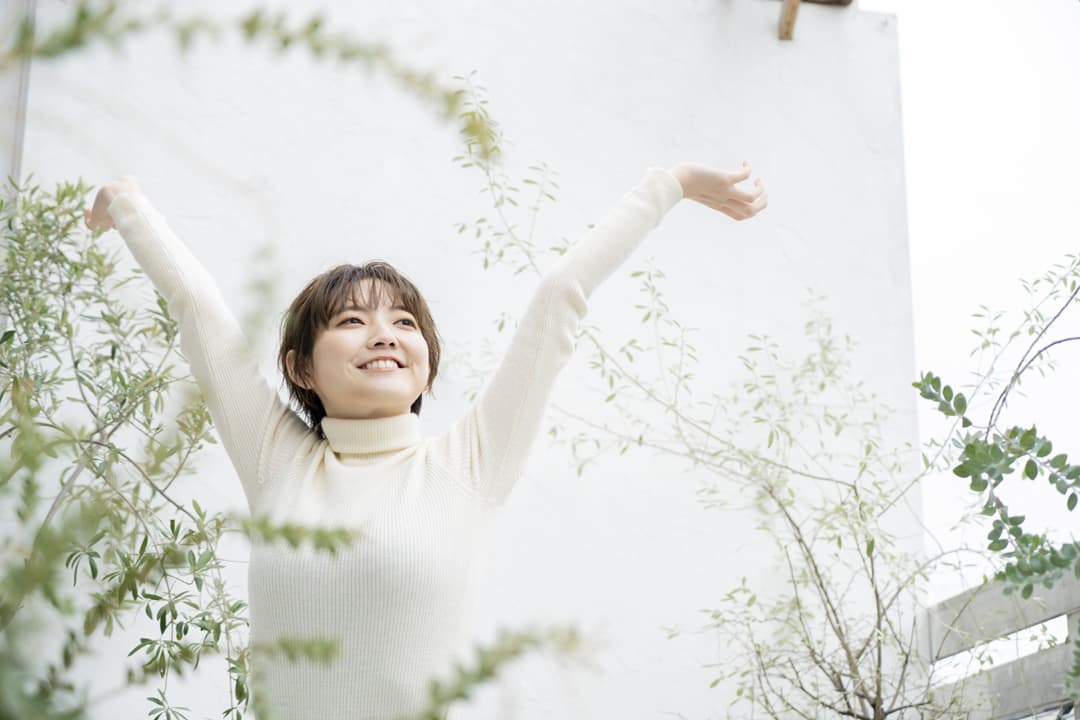 自然体で笑顔を見せ、両手を伸ばしてリラックスする女性のイメージ。安心感や「自分らしさ」を取り戻したHSS型HSPの姿